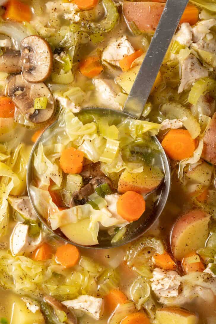 A pot of chicken and cabbage soup with vegetables. A ladle rests in the pot.