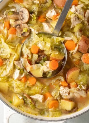 A white Dutch oven filled with Chicken Cabbage Soup.