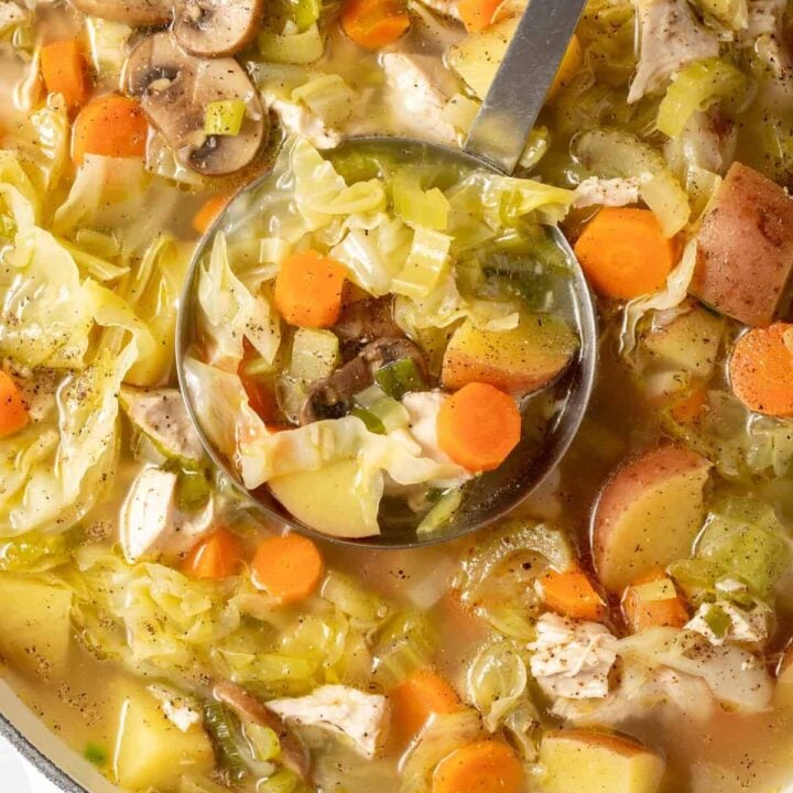 A white Dutch oven filled with Chicken Cabbage Soup.