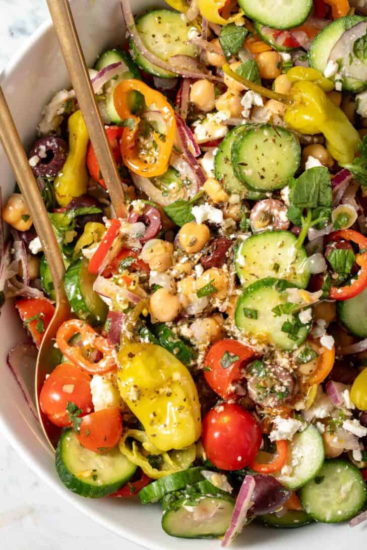 A white bowl filled with cucumber chickpea salad tossed with tomatoes, Feta cheese and Kalamata olives.