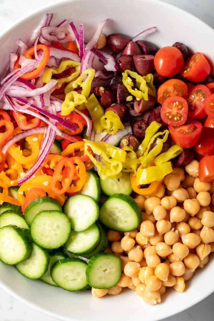 A white bowl filled with chopped vegetables for a Greek Chickpea Salad recipe.