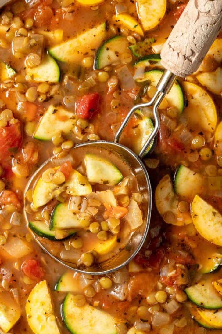 A pot of lentil vegetable soup with a ladle resting in the pot.