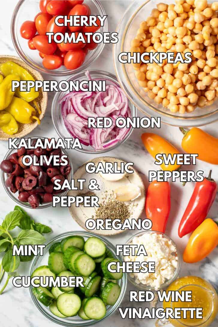 Class bowls filled with garbanzo beans, sliced cucumber, olives, onion and Feta cheese.