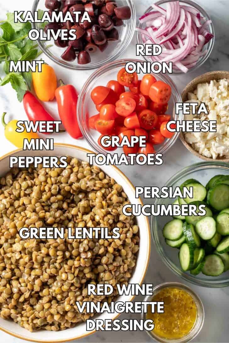 Glass bowls filled with legumes, sliced cucumbers, grape tomatoes, Feta cheese, sliced onion and kalamata olives.