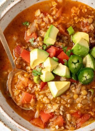 A bowl of Lentil Rice Soup garnished with chopped avocado, tomato, green onion and cilantro.