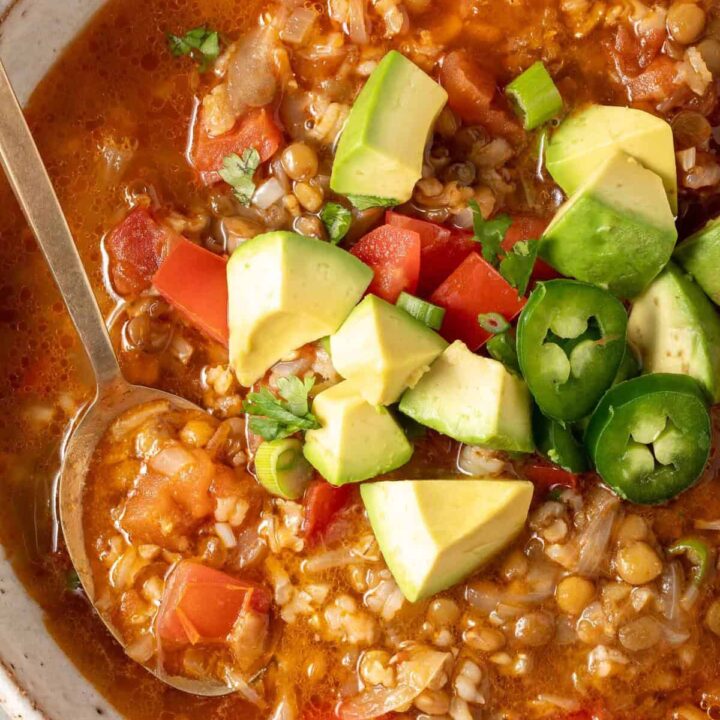 A bowl of Lentil Rice Soup garnished with chopped avocado, tomato, green onion and cilantro.