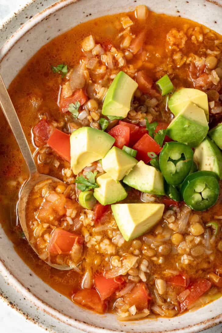 A bowl of lentil rice soup garnished with avocado, chopped tomatoes, green onion and cilantro.