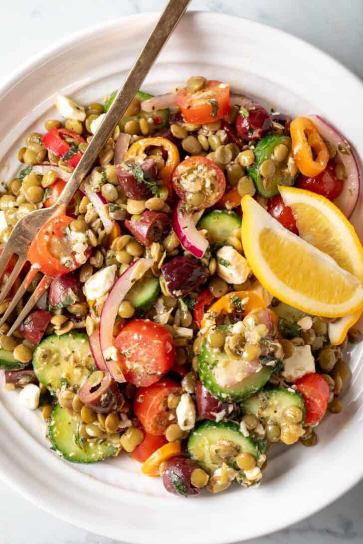A white bowl filled with the best lentil salad made with lentils, grape tomatoes, sliced cucumber, kalamata olives, red onion and Feta cheese.