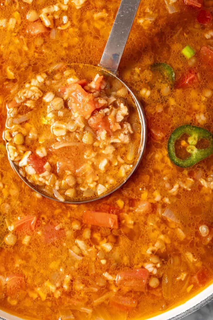 A white pot filled with Mexican Lentil Brown Rice Soup. A ladle rests in the pot.