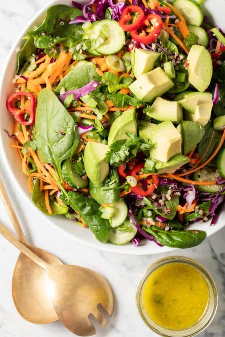 A bowl filled with Quinoa and Avocado Salad. A small glass bowl filled with dressing sits next to the bowl.
