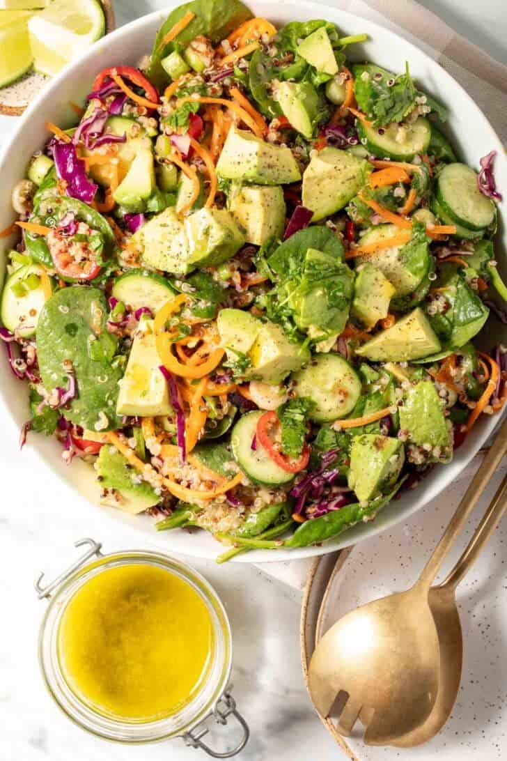 A bowl filled with quinoa avocado salad. A jar of vinaigrette sits next to the bowl.