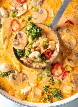A white Dutch oven filled with Tom Kha Gai Thai Coconut Chicken Soup with curry.