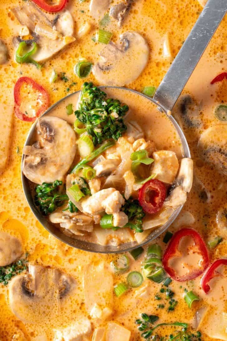 A pot of Tom Khal Gai Thai Coconut Curry Chicken Soup. A ladle rests in the pot filled with soup.