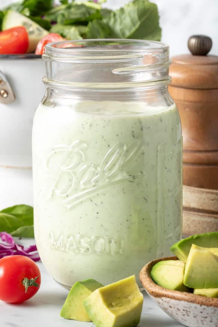 A clear glass mason jar filled with Avocado Ranch Dressing.