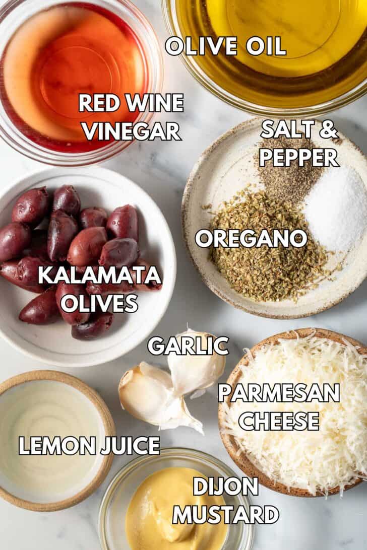 Small bowls filled with grated Parmesan cheese, dried oregano, red wine vinegar, olive oil, and mustard for a Greek Vinaigrette Dressing.