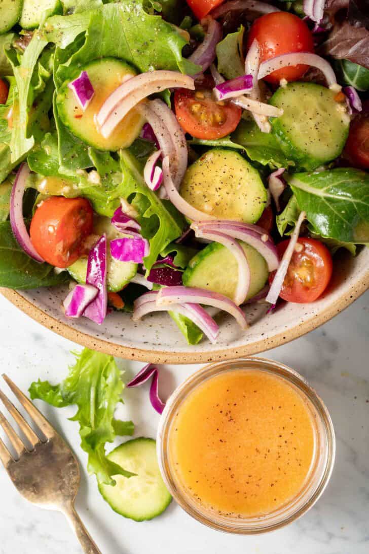 A small glass jar filled with Chipotle Vinaigrette sits next to a bowl of salad.