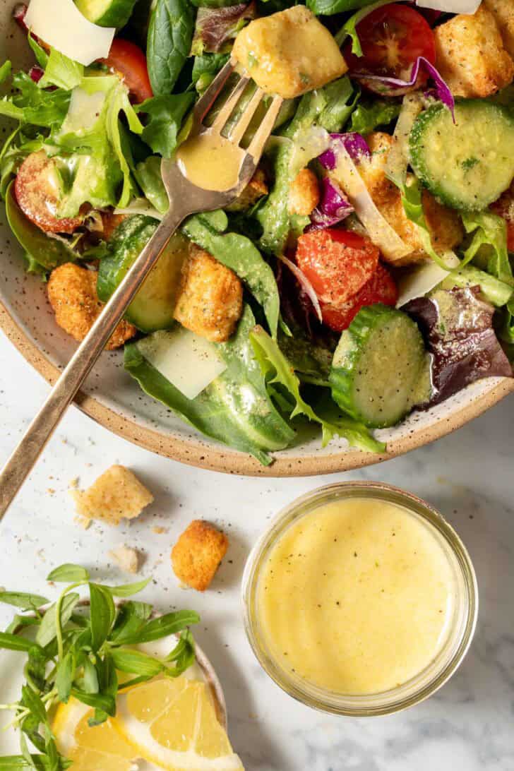 A bowl of salad tossed with Tarragon Salad Dressing. A small jar of dressing sits next to the salad.