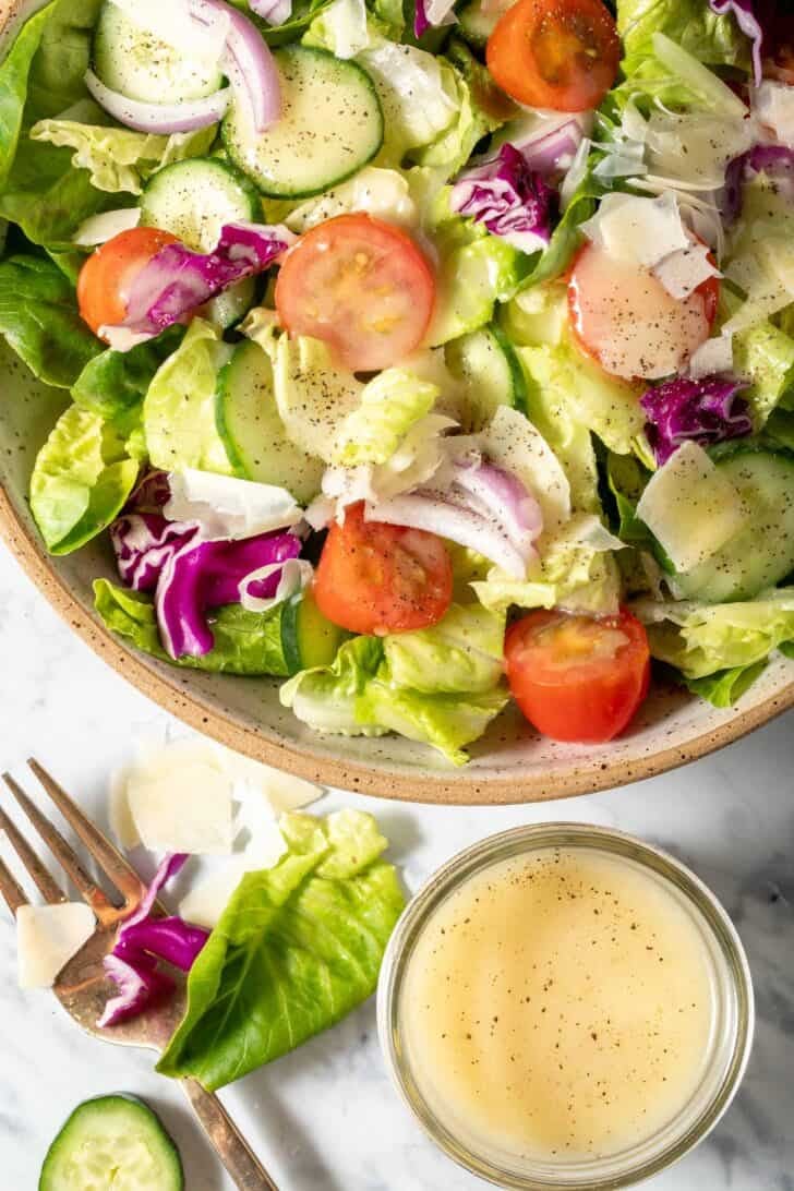 A bowl filled with salad tossed with White Balsamic Vinaigrette Dressing. A small glass jar filled with dressing sits next to the bowl.