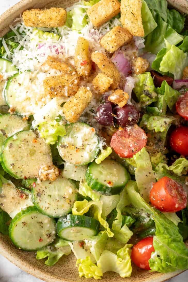 A plate filld with salad tossed with Creamy Italian Salad Dressing.