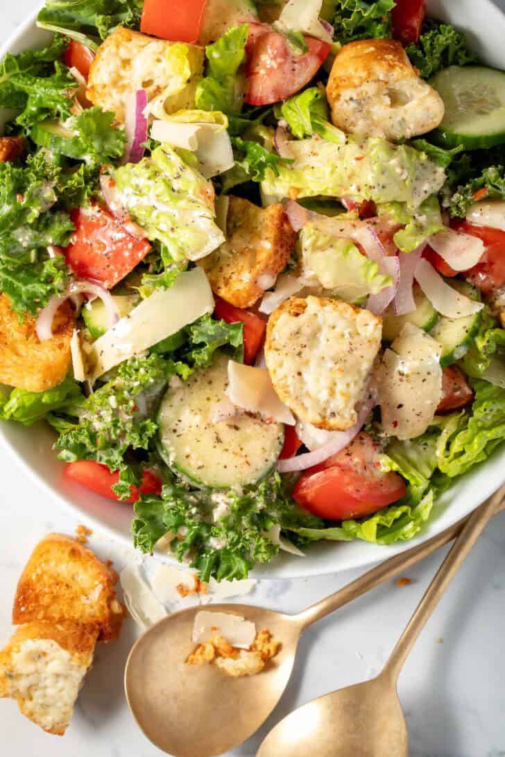 A white bowl with Simple Kale Salad tossed with gorgonzola croutons.