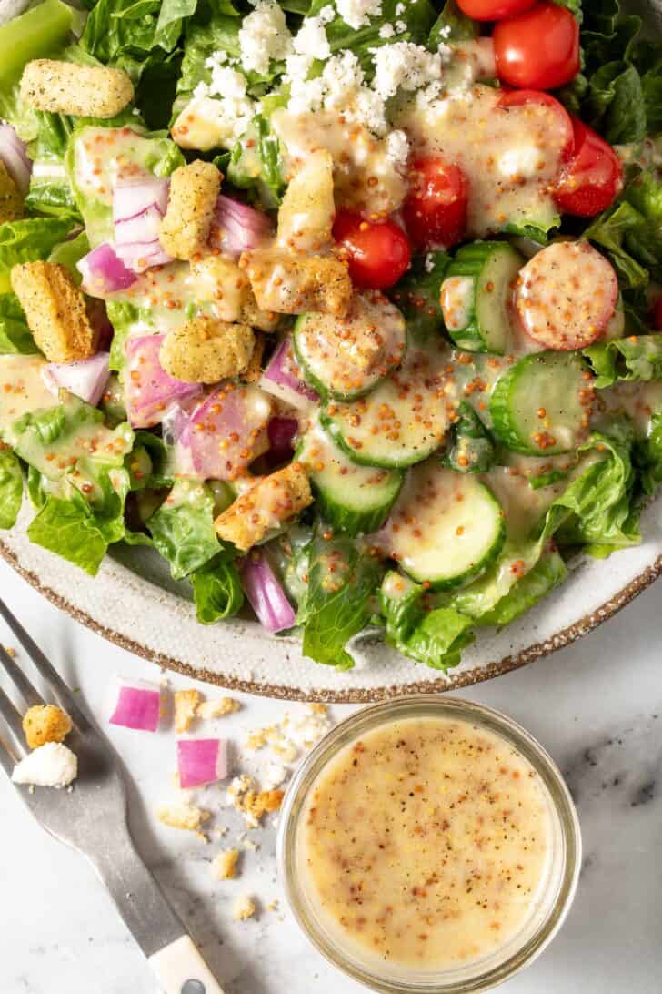 A bowl filled with a leafy green salad tossed with homemade Honey Mustard Salad Dressing.