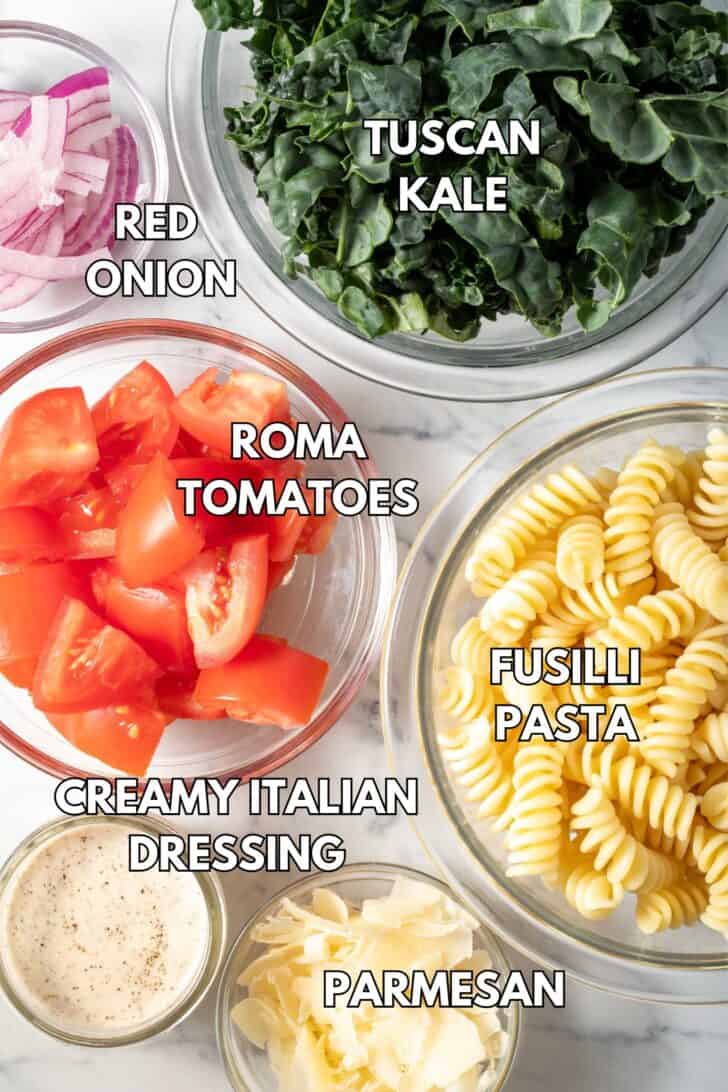 Clear glass bowls filled with lttuce, tomatoes, red onion, cheese and noodles.