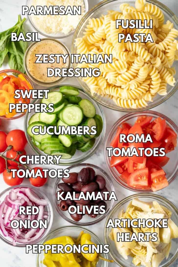 Glass bowls filled with noodles, tomatoes, cucumbers, olives, cheese and onions.