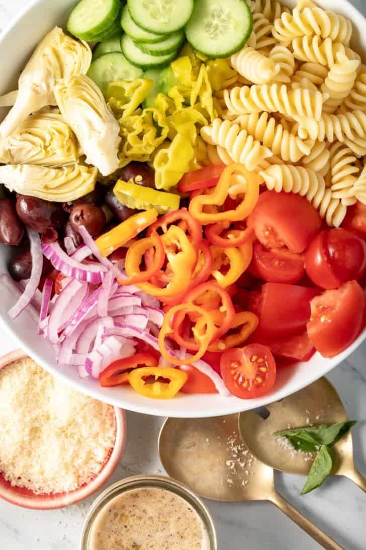 A white bowl filled with noodles, tomatoes, sliced onion, olives, and cucumbers for a Pasta Salad Recipe with Italian Dressing.