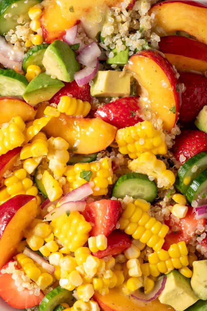 A white bowl filled with easy Summer Quinoa Salad with nectarines, strawberries, and corn on the cob.