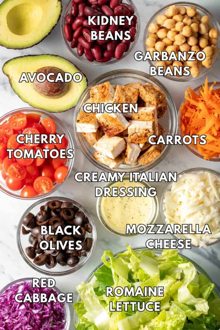 Clear glass bowls filled with chicken, lettuce, cheese, beans and tomatoes.