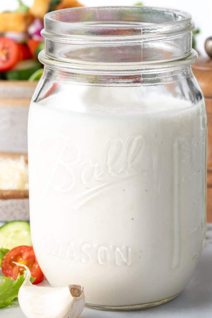 A clear mason jar filled with Creamy Garlic Salad Dressing.