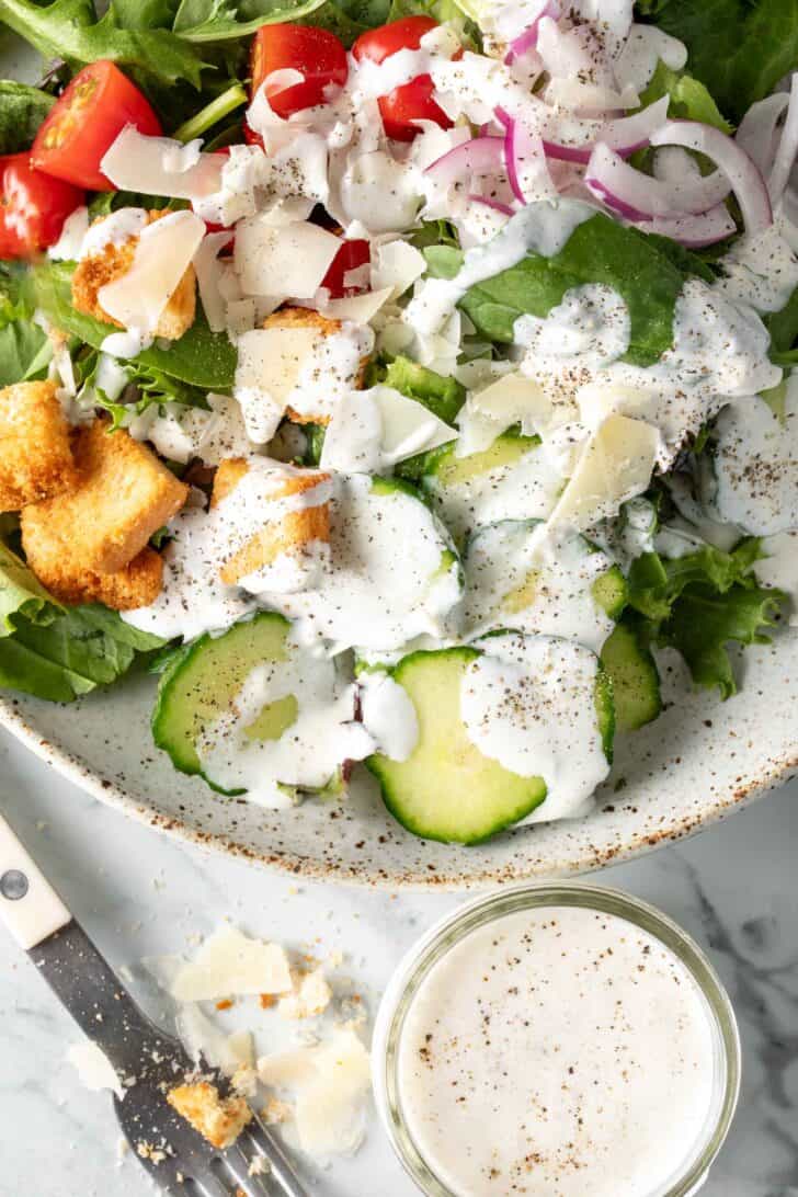 A white bowl filled with salad tossed with Creamy Garlic Parmesan Dressing.