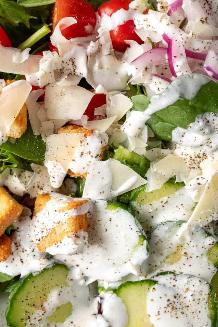 A white plate filled with salad tossed with homemade Creamy Garlic Salad Dressing.