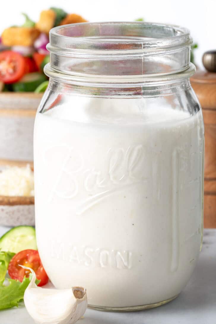 A clear mason jar filled with Creamy Garlic Dressing.