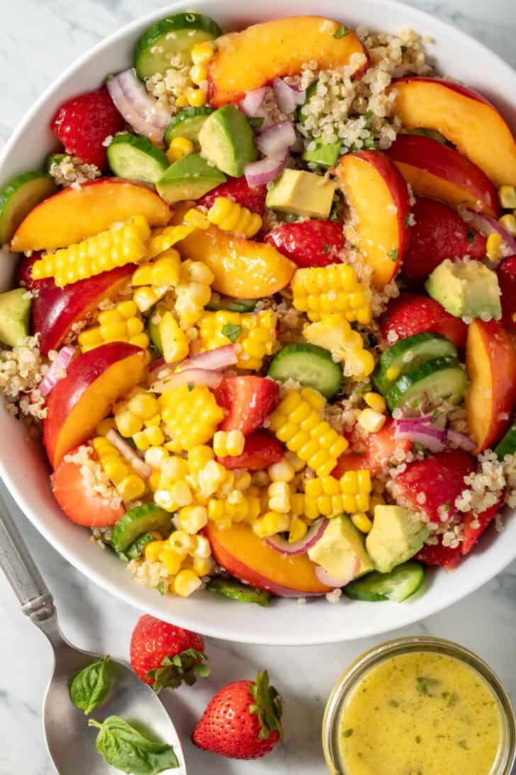 A white bowl filled with Summer Quinoa Salad (with nectarines, strawberries and corn on the cob).