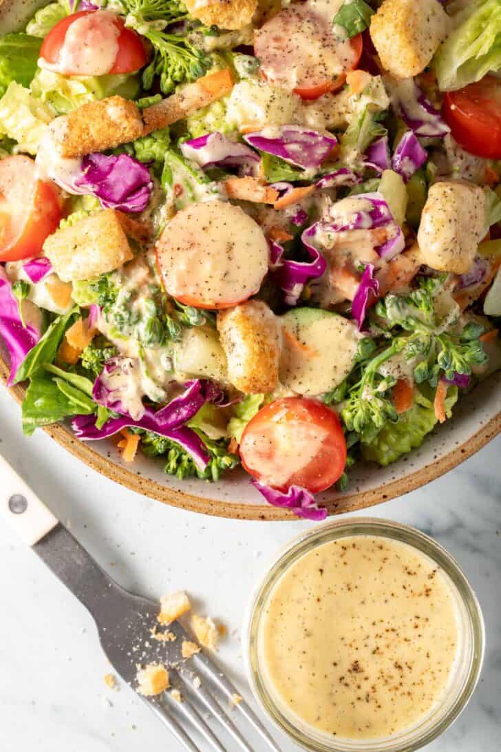 A white bowl filled with salad tossed with Creamy Vinaigrette Salad Dressing.