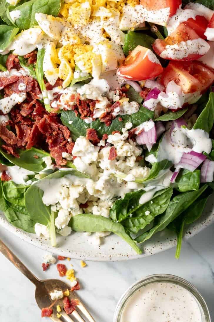 A white plate filled with Spinach and Bacon Salad.