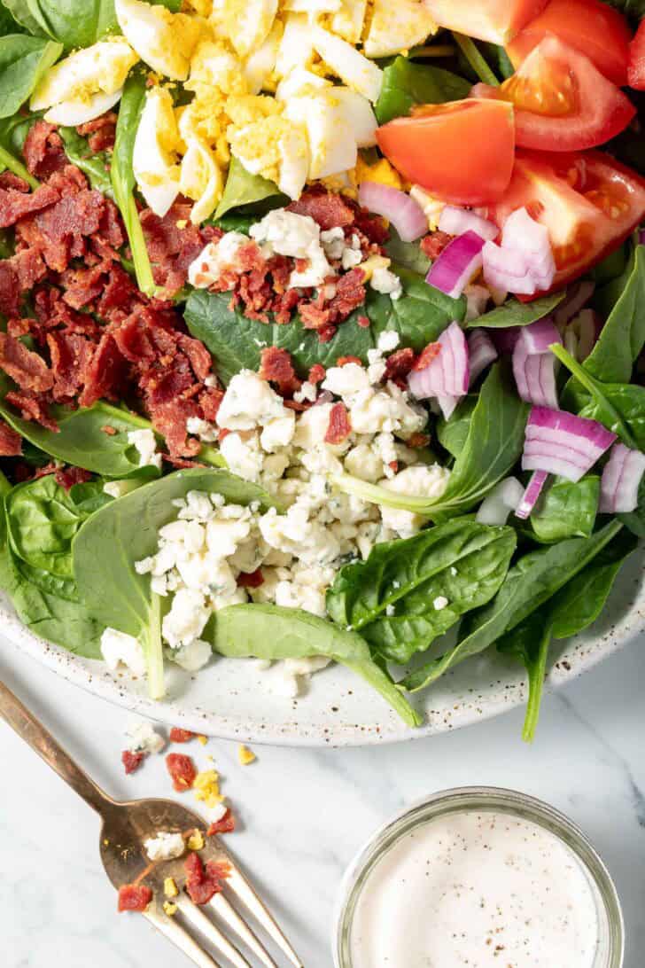 A white plate filled with Spinach Bacon Salad.