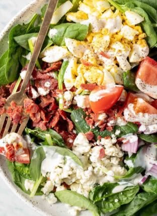A white plate filled with Bacon Spinach Salad.
