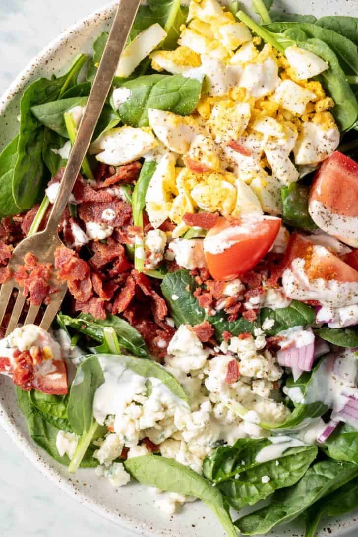 A white plate filled with Spinach and Bacon Salad.