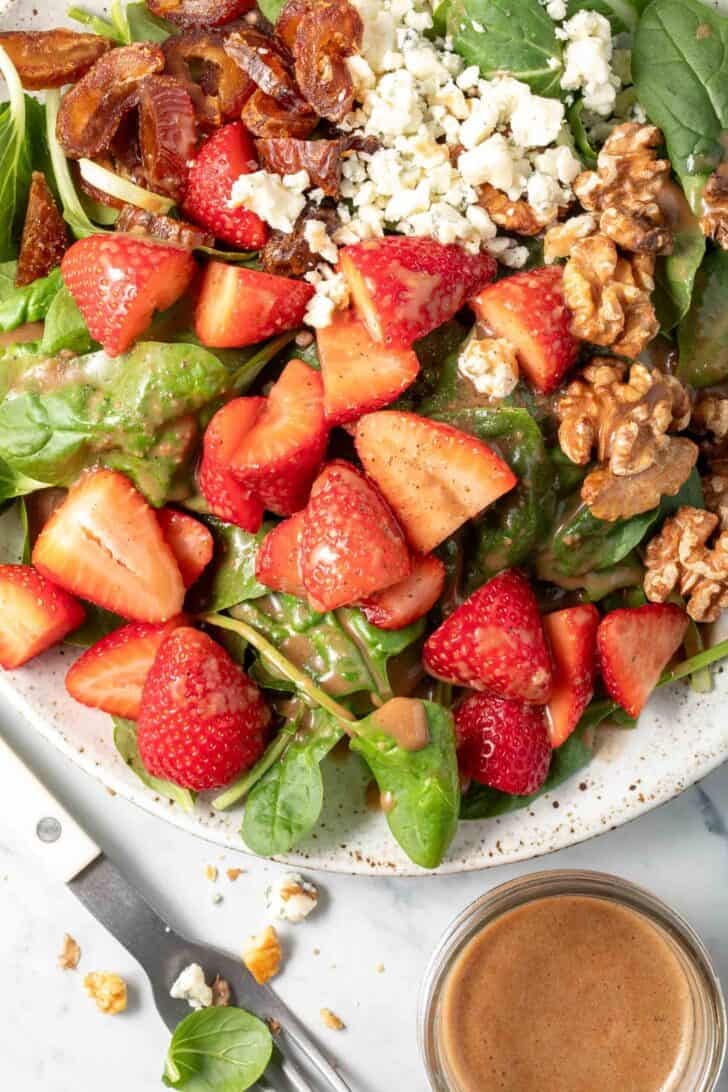 A white plate filled with spinach salad with strawberries.