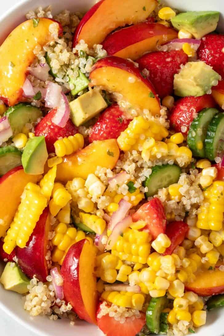 A white bowl filled with the best Summer Quinoa Salad with nectarines, strawberries and corn on the cob.