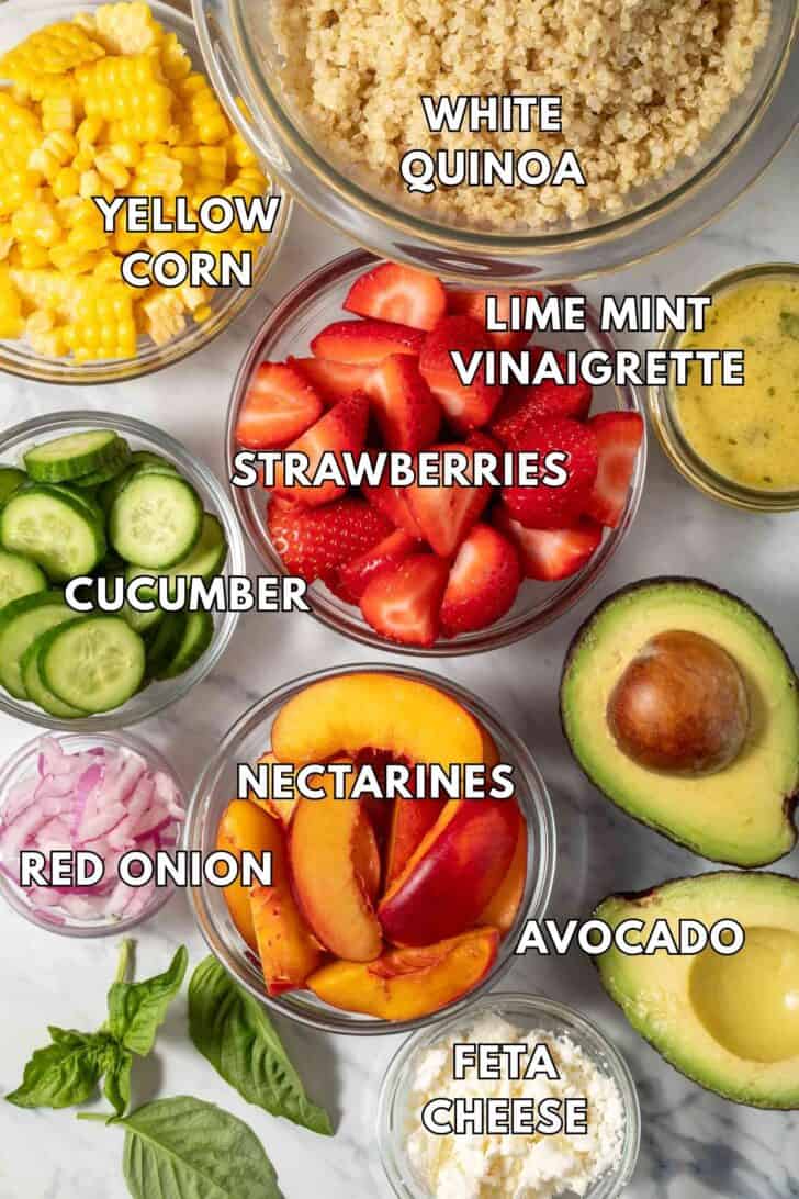 Clear glass bowls filled with strawberries, nectarines, red onion, cucumbers and yellow corn.