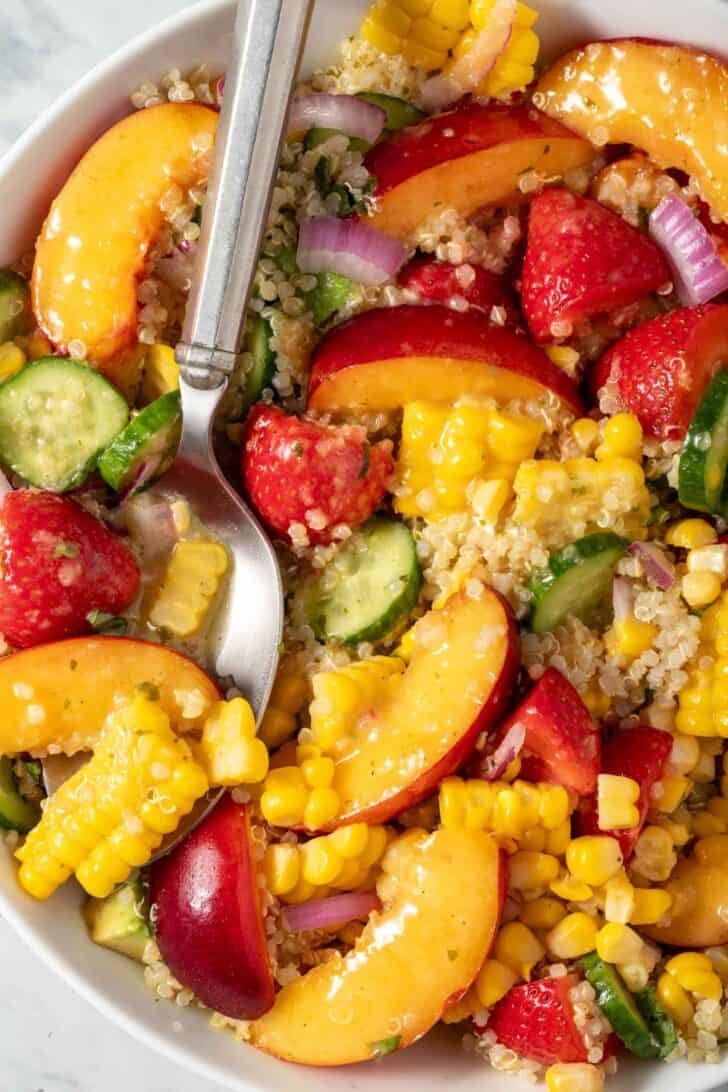 A white bowl filled with Summer Quinoa Salad with nectarines, strawberries and corn on the cob.