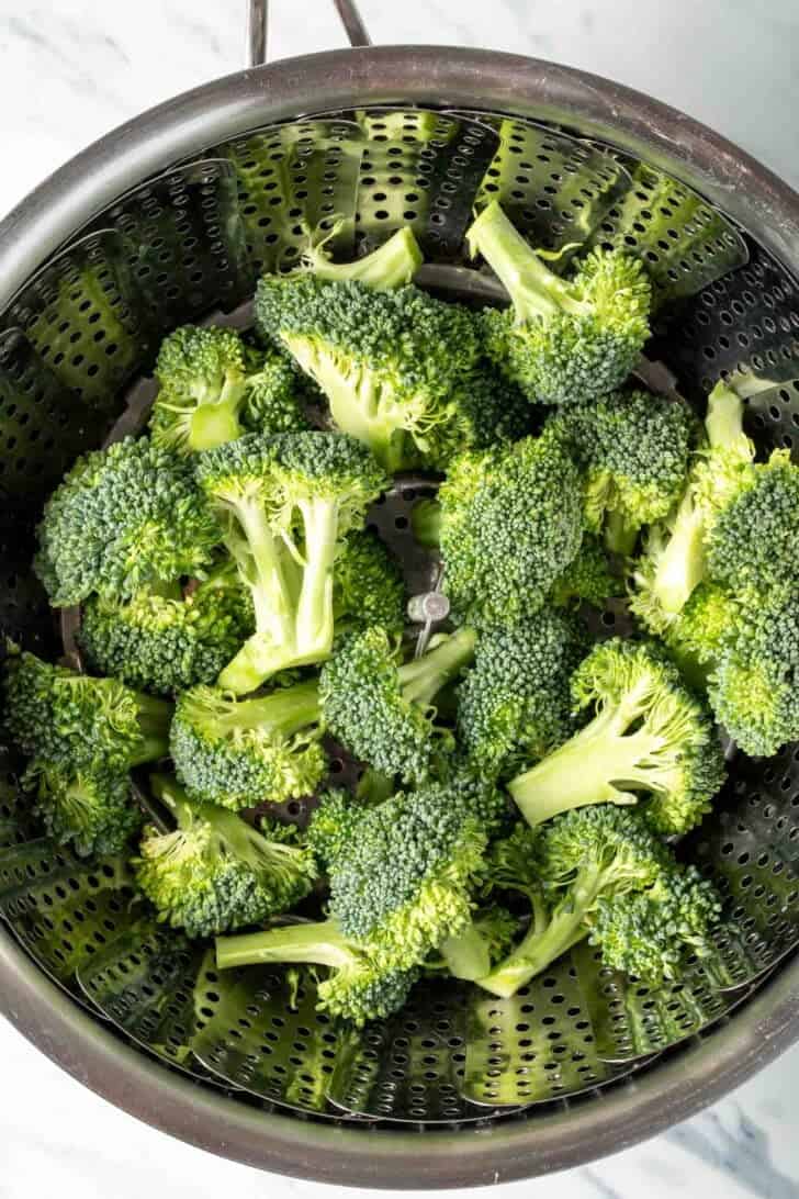 Raw broccoli in a steamer basket inside a pot.