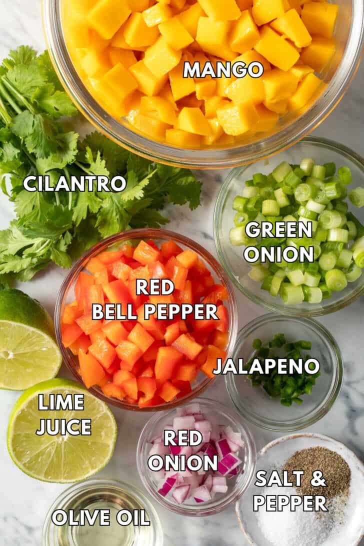 Clear glass bowls filled with chopped fruit, red bell pepper, green onion, red onion and jalapeno.