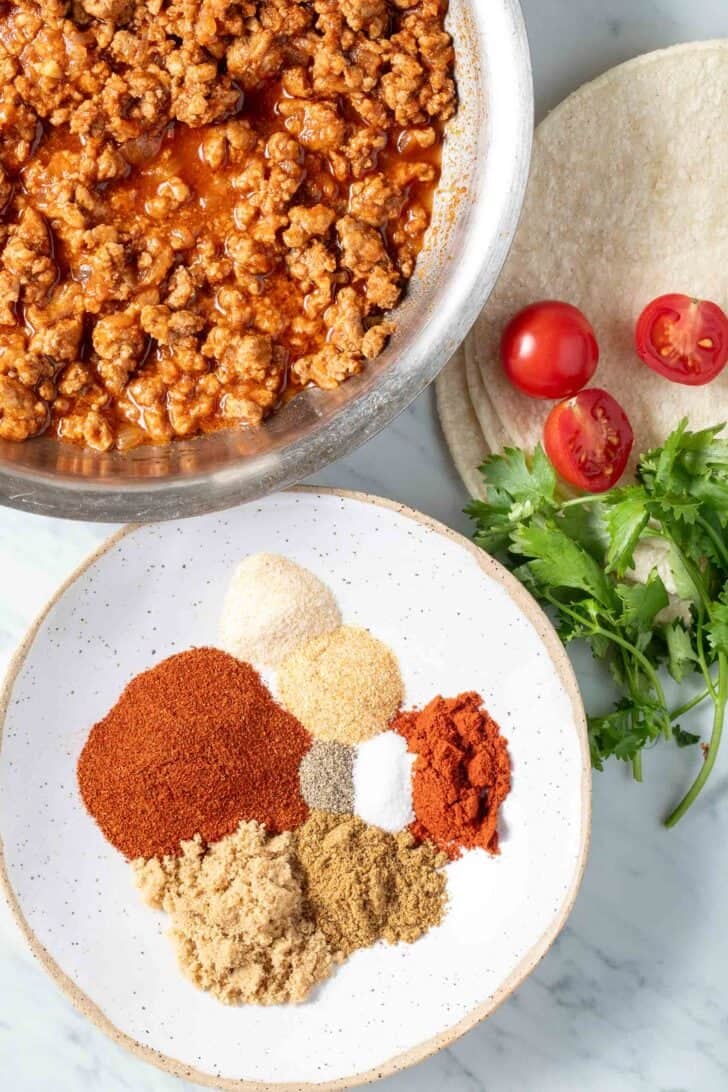 Mild Taco Seasoning on a white dish next to a skillet of taco meat.