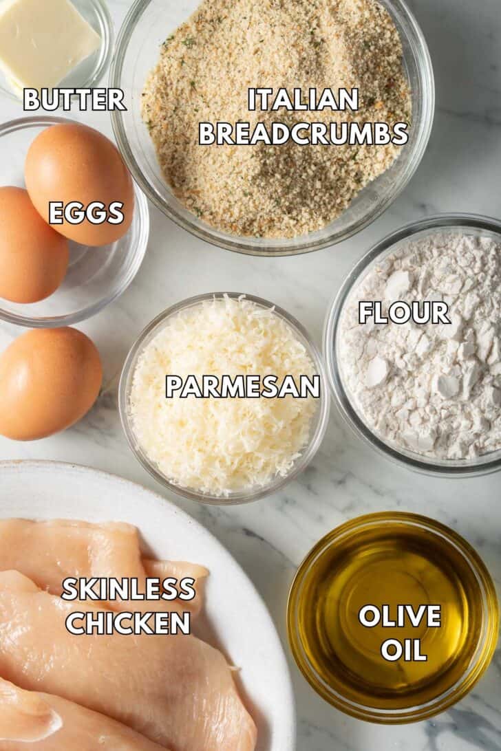 Clear glass bowls filled with breadcrumbs, flour, Parmesan cheese, eggs, olive oil and butter.