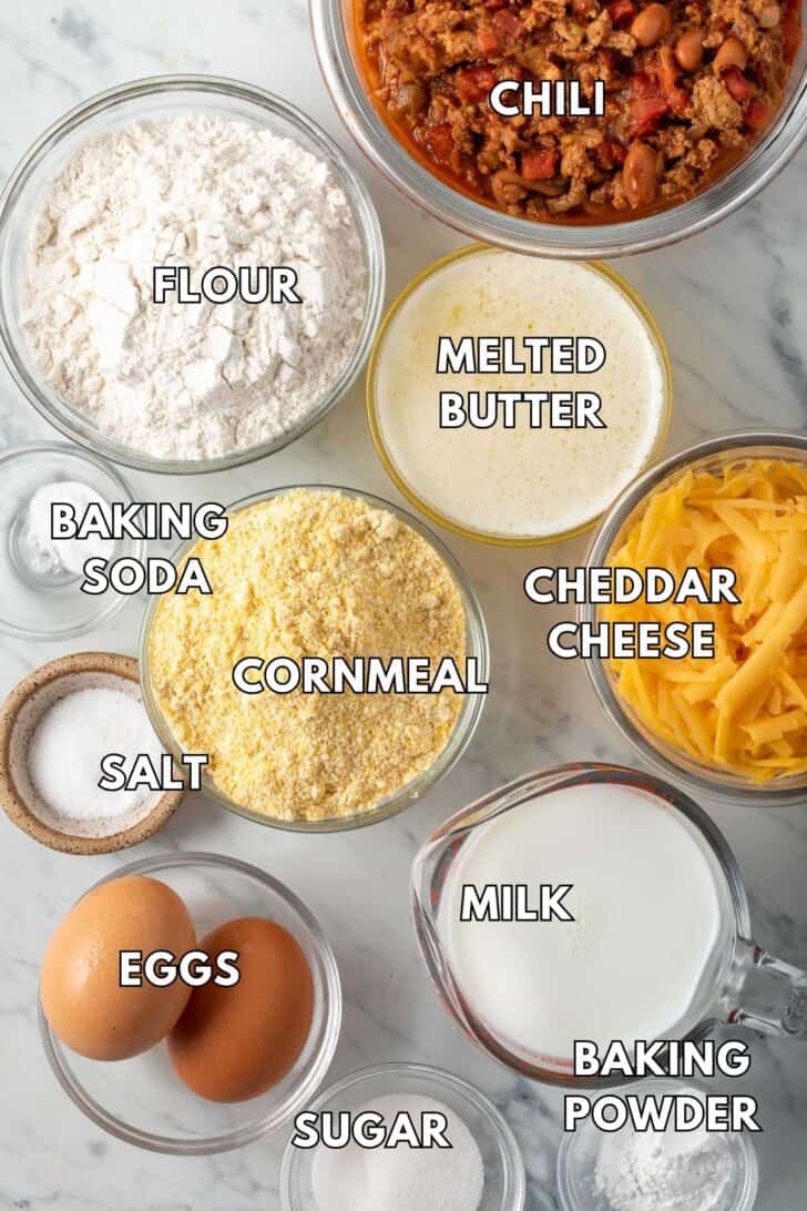 Clear glass bowls filled with flour, melted butter, cornmeal, milk, and eggs.