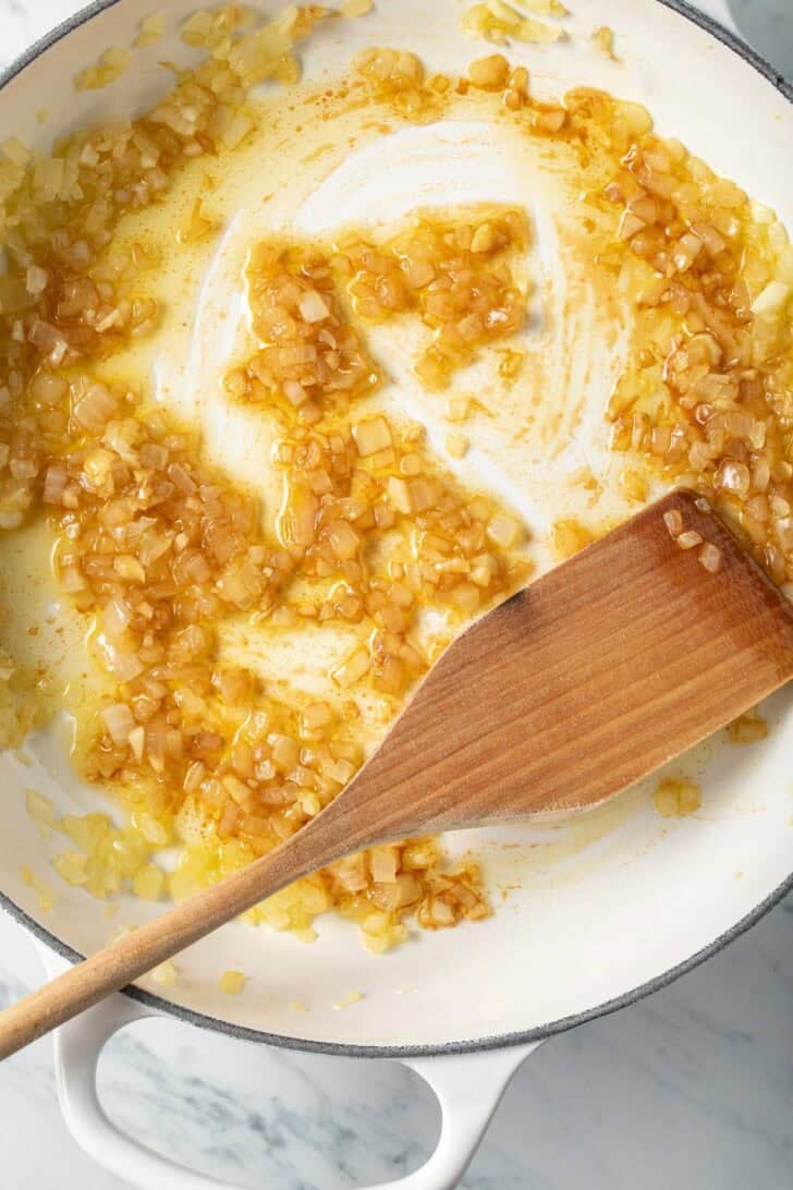 Cooked onions in a skillet with a wooden spoon.